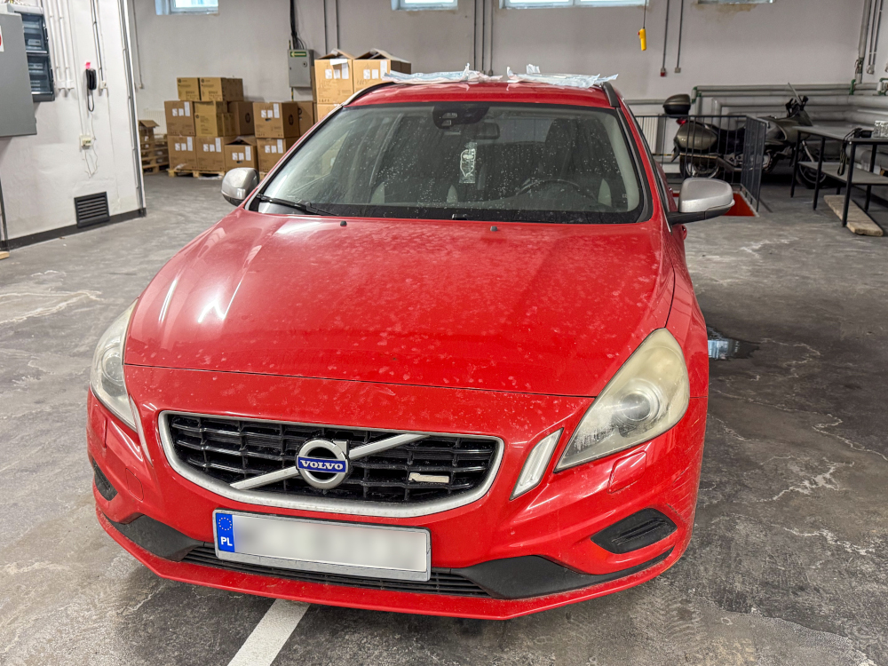 Czerwony samochód marki Volvo zaparkowany w pomieszczeniu z widocznymi kartonami w tle.