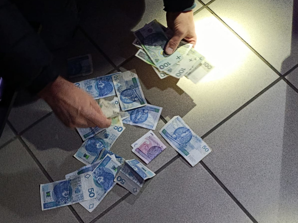 Mężczyzna zbiera banknoty leżące na podłodze w oświetlonym pomieszczeniu.