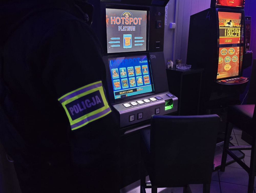Funkcjonariusz policji stoi obok automatu do gier w ciemnym pomieszczeniu, na którym widnieje napis "HOTSPOT".