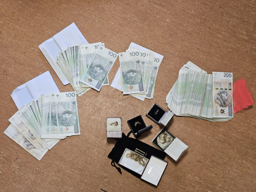 Na podłodze leżą stosy banknotów, w tym setki i dwieście złotych, obok biżuteria w eleganckich pudełkach.