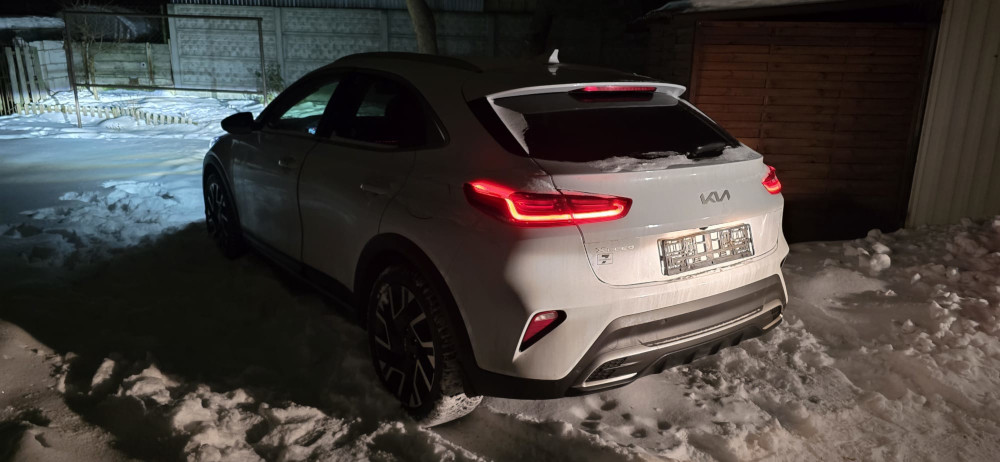 Biały samochód osobowy zaparkowany na zaśnieżonym terenie nocą, oświetlony przez latarnię.