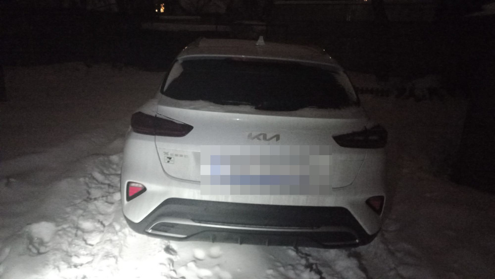 Biały samochód zaparkowany na śniegu w ciemnym otoczeniu, z widocznymi śladami opon wokół.