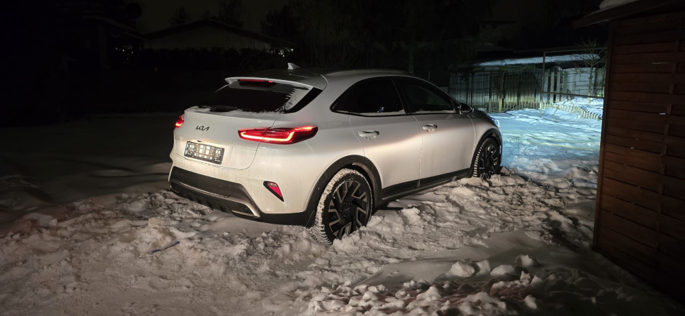 Biały samochód osobowy zaparkowany na zaśnieżonym terenie nocą, w tle widoczny oświetlony chodnik.