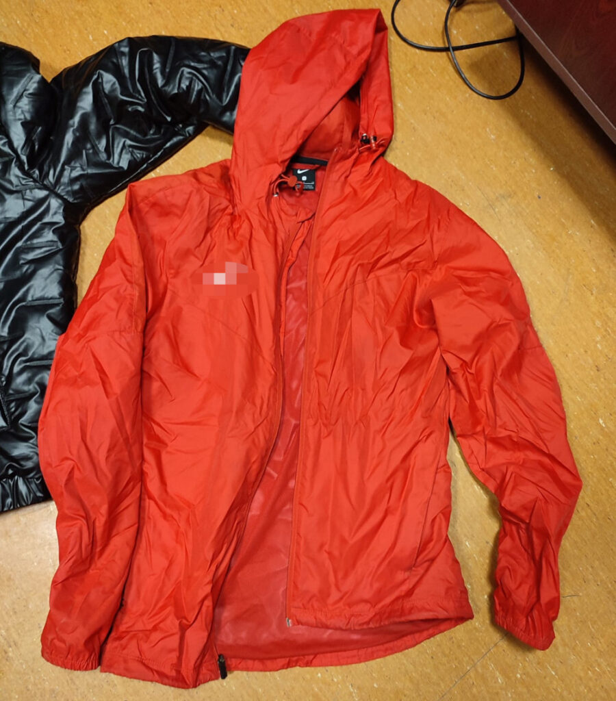 Czerwona kurtka z kapturem leży na drewnianej podłodze obok czarnej kurtki.