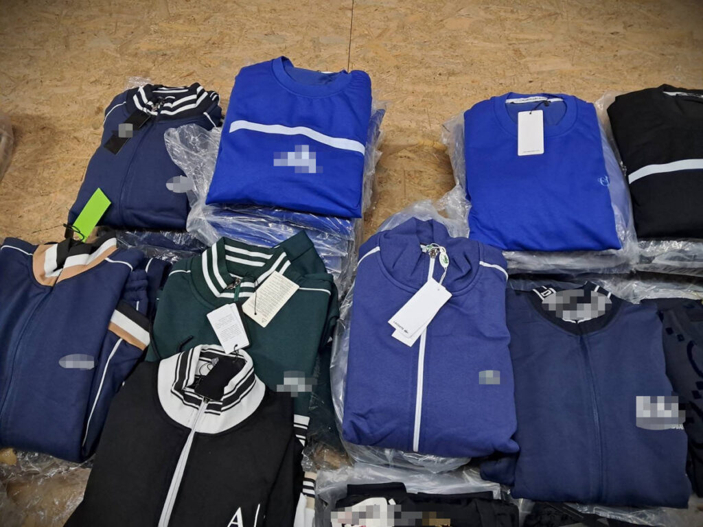 Zestaw odzieży sportowej w różnych kolorach, ułożony na drewnianej powierzchni, z widocznymi metkami.