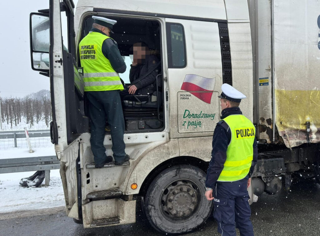 Funkcjonariusze Inspekcji Transportu Drogowego rozmawiają z kierowcą ciężarówki w zimowej scenerii.