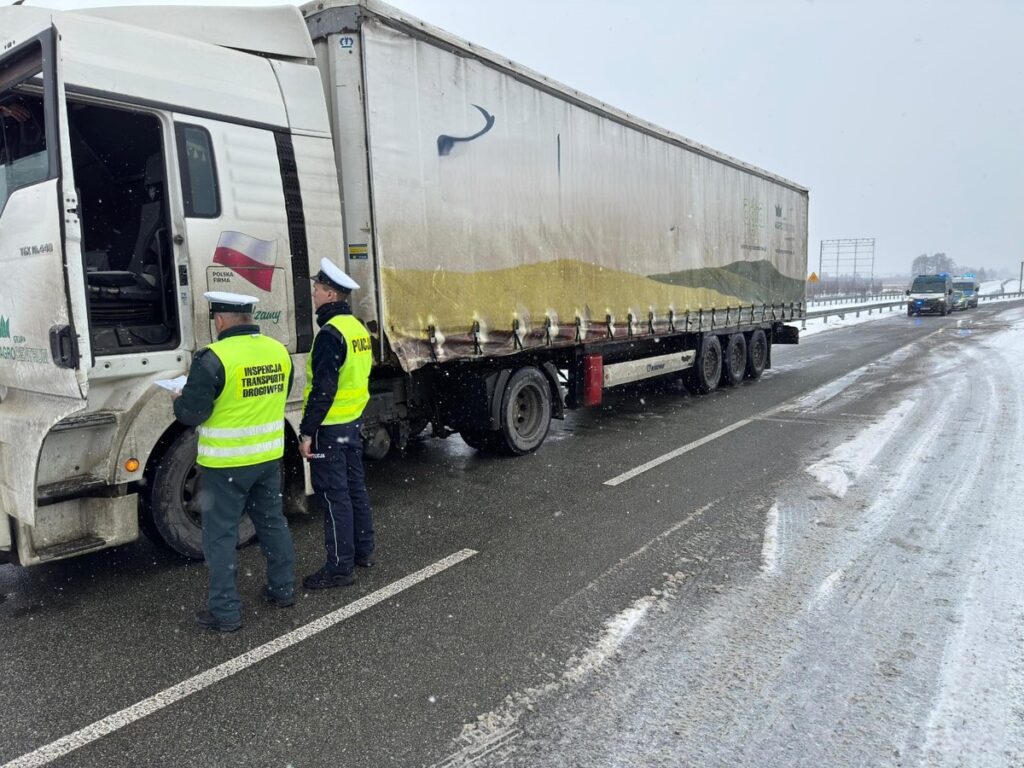 Funkcjonariusze Inspekcji Transportu Drogowego kontrolują ciężarówkę na zaśnieżonej drodze.