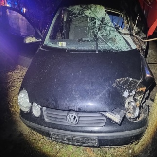 Uszkodzony czarny samochód osobowy marki Volkswagen z wgniecionym przodem, leżący na poboczu drogi.