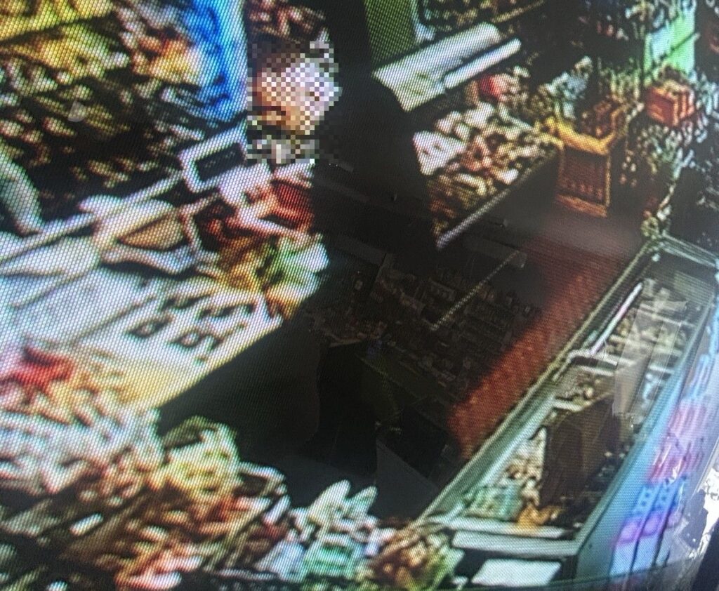 Mężczyzna w sklepie spożywczym obsługujący klientów przy ladzie z różnymi produktami.