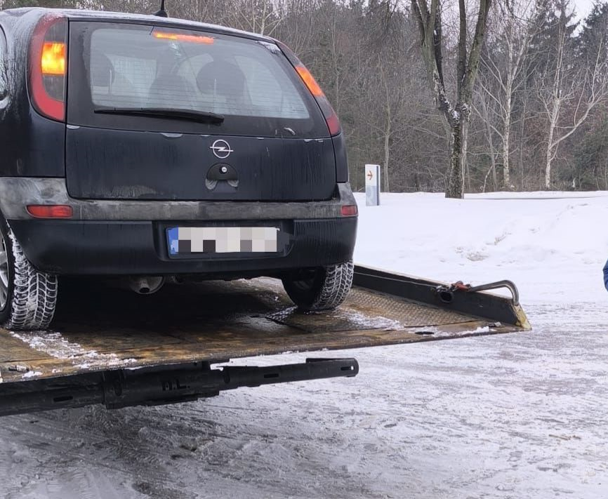 Czarny samochód osobowy marki Opel wciągany na lawetę w zimowym otoczeniu z zaśnieżoną nawierzchnią.