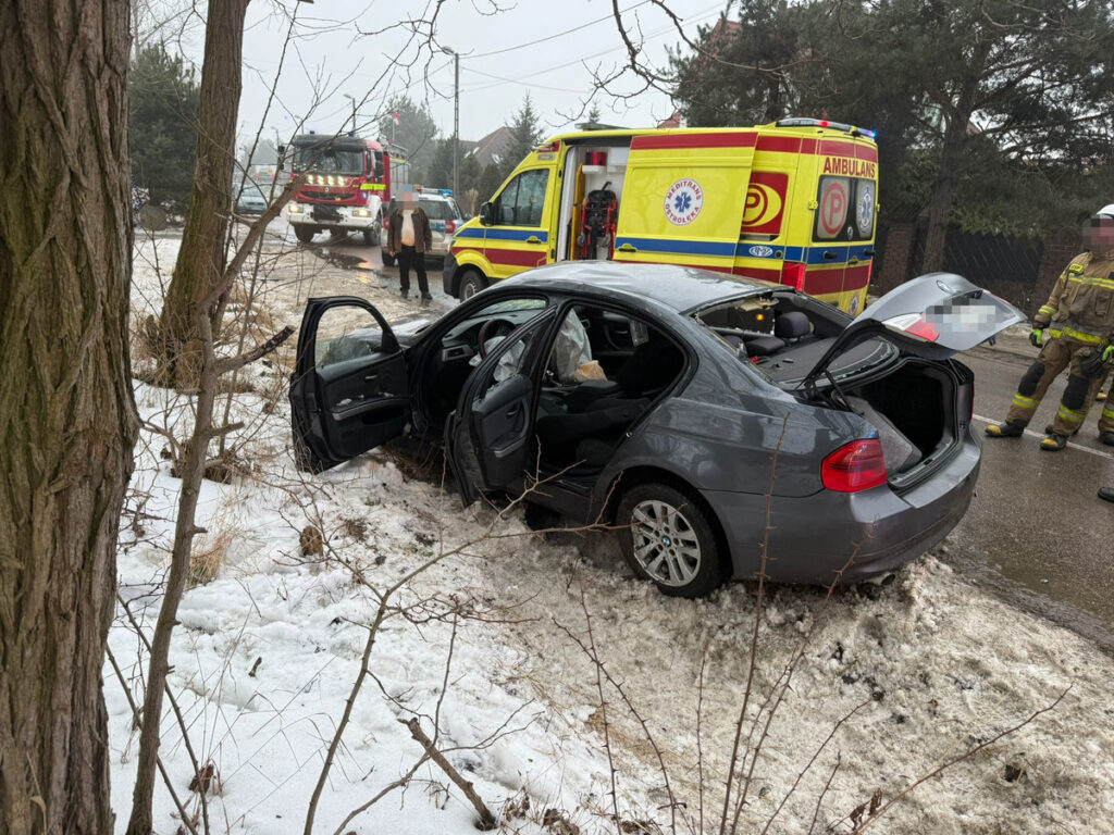 Samochód osobowy w rowie, otoczony przez zespół ratunkowy i strażaków, w zimowej scenerii z śniegiem.