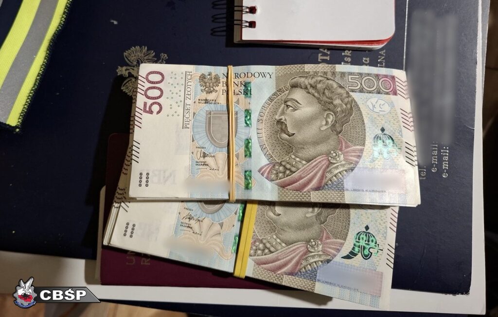 Pieniądze w nominałach 500 zł ułożone na stole obok notesu i paszportu, z widoczną gumką do trzymania.