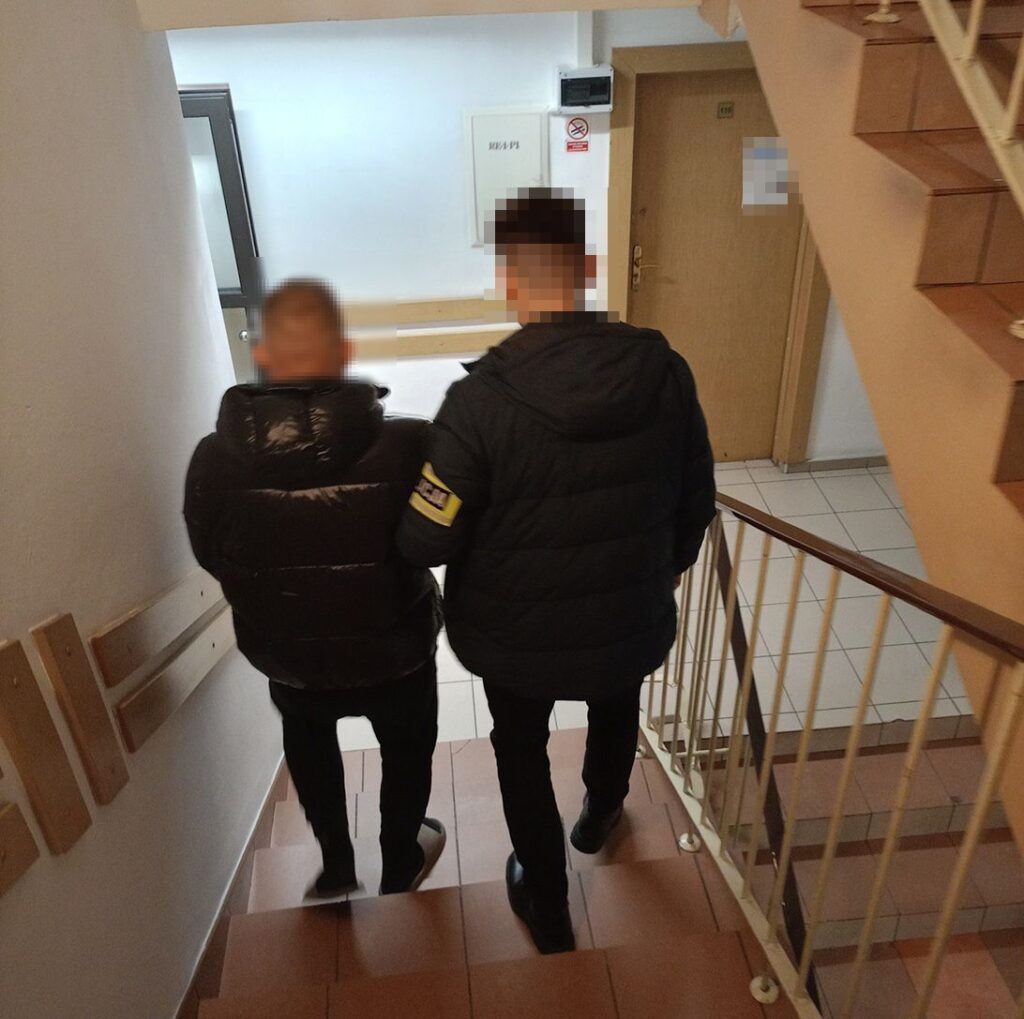 Dwaj mężczyźni w kurtkach puchowych schodzą po schodach w budynku, trzymając się za ręce.