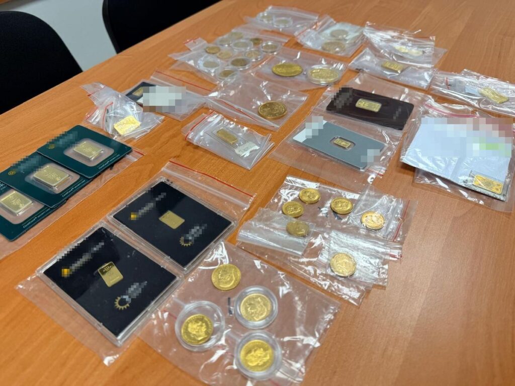 Zestaw złotych sztabek i monet umieszczonych w przezroczystych woreczkach na drewnianym biurku.