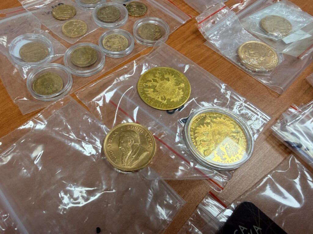 Złote monety umieszczone w przezroczystych kopertach na drewnianym blacie.