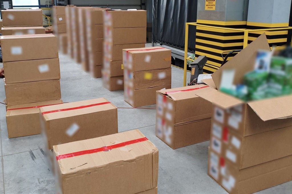 Pakiety w kartonowych pudłach ułożone na podłodze w magazynie, część z nich otwarta.