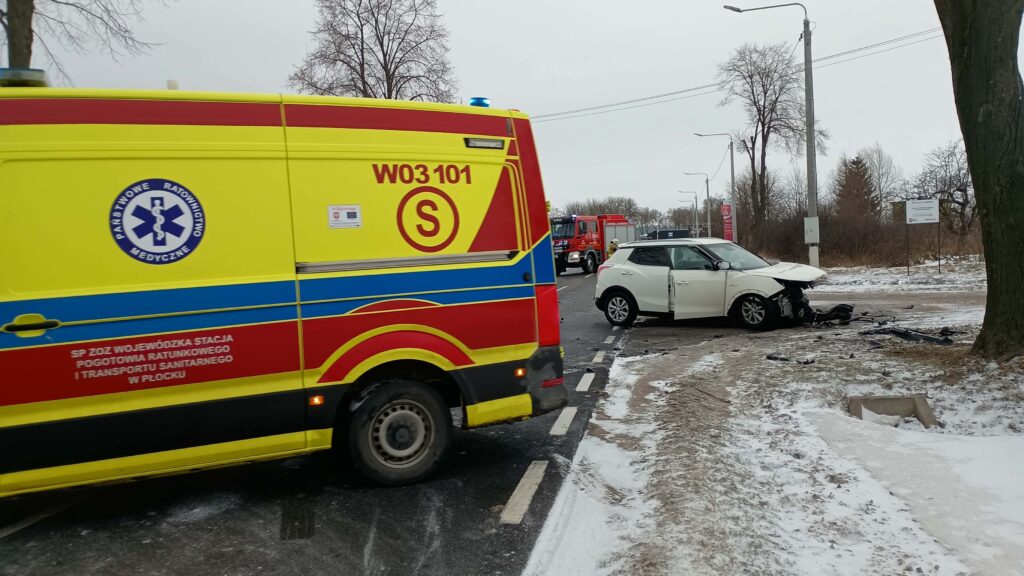 Ambulans ratunkowy zatrzymany obok uszkodzonego białego samochodu osobowego na ośnieżonej drodze.