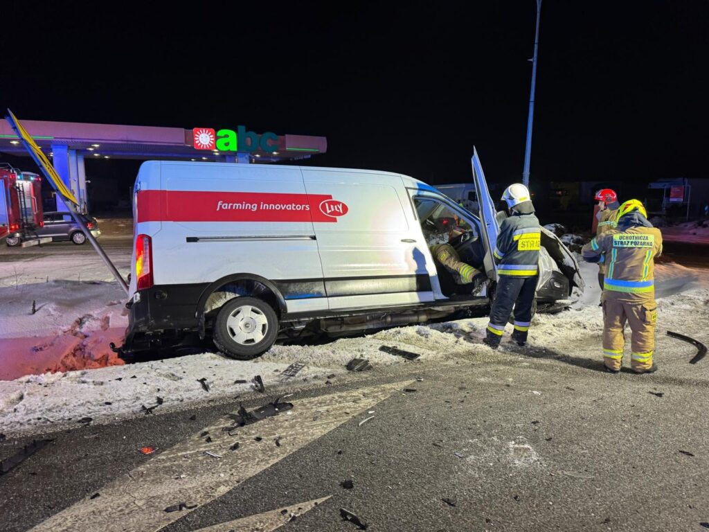 Samochód dostawczy w rowie, a strażacy udzielają pomocy wewnątrz pojazdu w nocy obok stacji benzynowej.