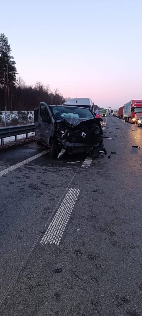 Zniszczony samochód dostawczy na drodze, wokół widać inne pojazdy i znaki ostrzegawcze.