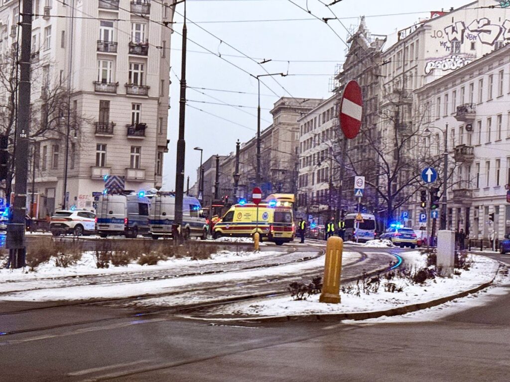 Policyjny i ratunkowy pojazd z włączonymi sygnałami świetlnymi na zaśnieżonej ulicy, obok budynków mieszkalnych.