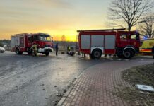 Strażacy pracują przy wypadku drogowym, obok dwóch wozów strażackich na skrzyżowaniu o zachodzie słońca.