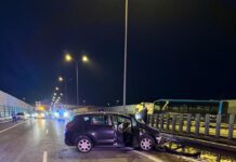 Czarny samochód osobowy z otwartymi drzwiami stoi na pasie ruchu, obok widać pojazdy służb ratunkowych.