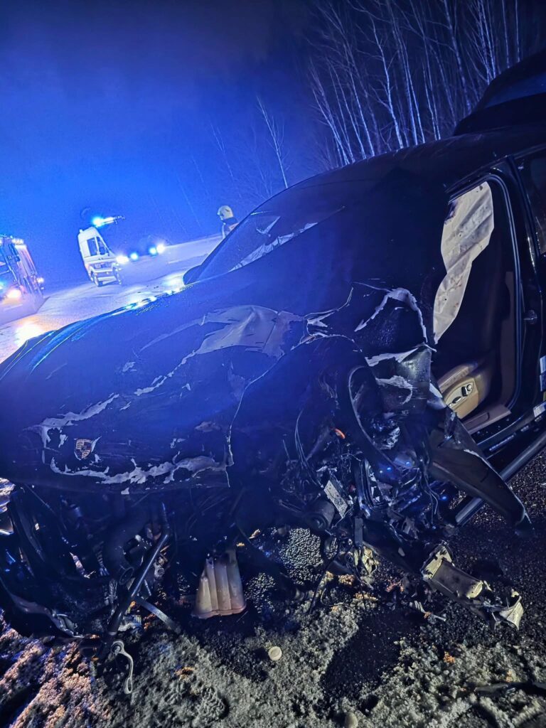 Zniszczony pojazd leży na poboczu drogi, otoczony przez niebieskie światła pojazdów służb ratunkowych w nocy.