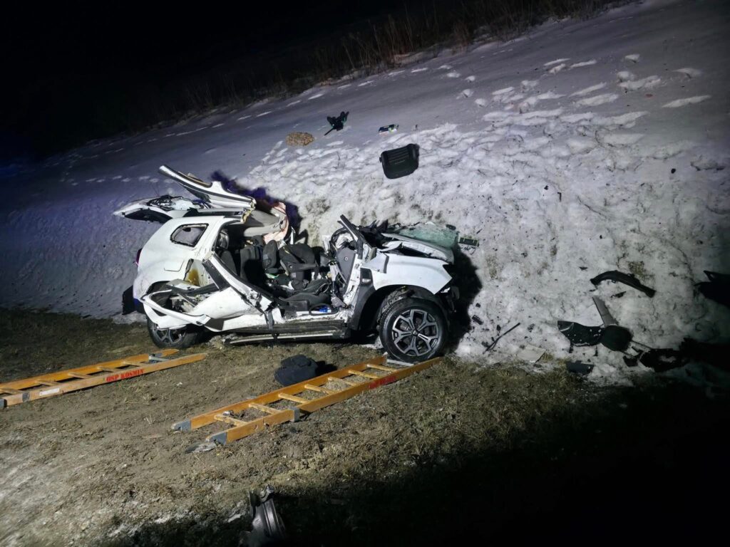 Zniszczony biały samochód osobowy leży na poboczu w pobliżu śnieżnego wzniesienia, obok drewniane deski ratunkowe.