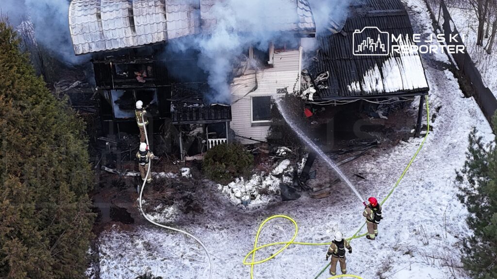 Strażacy gaszą pożar zniszczonego budynku, otoczonego dymem i śniegiem, przy użyciu węży gaśniczych.