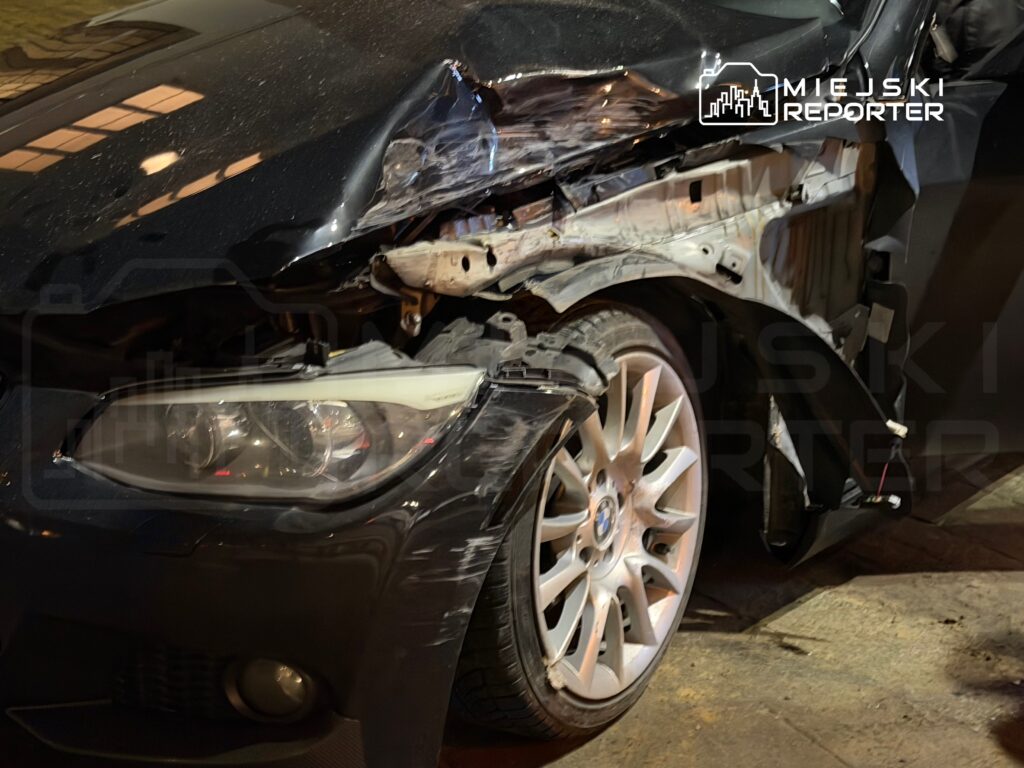 Uszkodzony samochód osobowy z wgniecioną karoserią i uszkodzoną lampą przednią zaparkowany na ulicy.