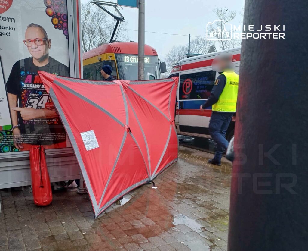 Mężczyzna w kamizelce odblaskowej przeprowadza interwencję obok czerwonego namiotu na przystanku tramwajowym.
