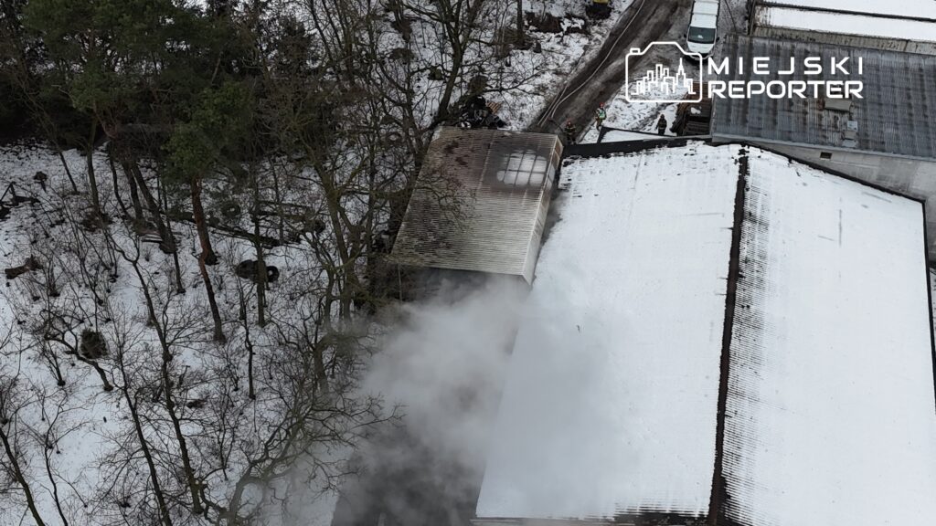 Dym wydobywający się z dachu budynku w otoczeniu ośnieżonego terenu i drzew.