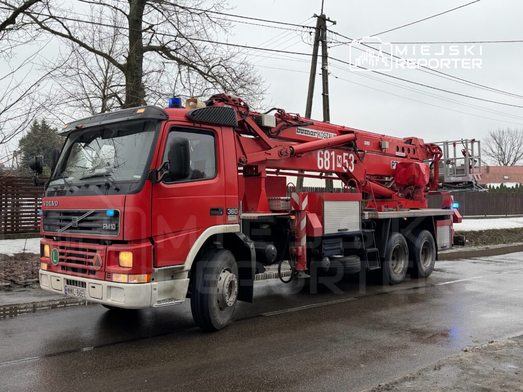 Czerwony wóz strażacki marki Volvo z podnośnikiem, zaparkowany przy ulicy w zimowym otoczeniu.