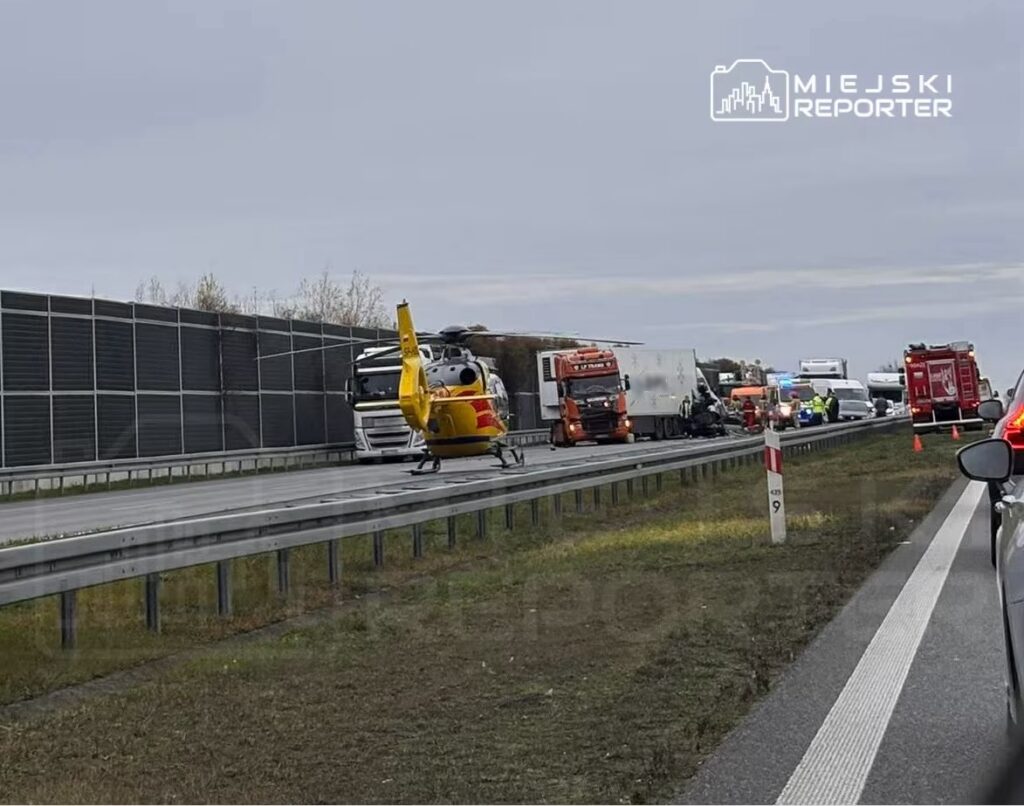 Śmigłowiec ratunkowy ląduje obok zablokowanej drogi, gdzie trwa akcja ratunkowa po wypadku drogowym z udziałem ciężarówek.