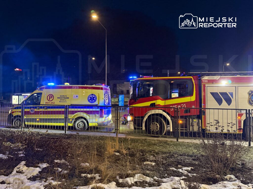 Ambulans i wóz strażacki zaparkowane przy ulicy w nocy, z włączonymi sygnałami świetlnymi.