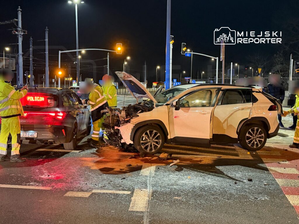 Policjanci w odblaskowych strojach badają miejsce wypadku drogowego, gdzie doszło do zderzenia dwóch samochodów.