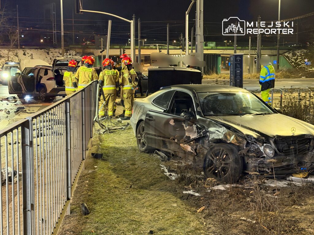 Grupa strażaków w mundurach ratunkowych pracuje przy zniszczonych samochodach po wypadku drogowym w nocy.