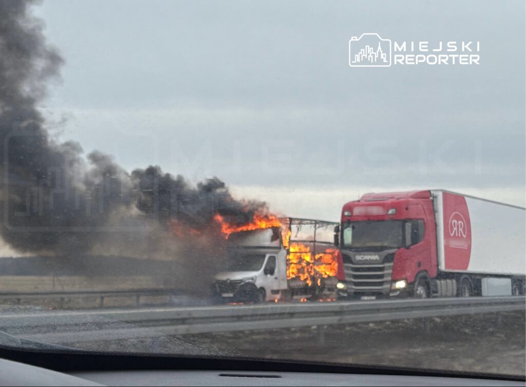 Czarny dym i płomienie wydobywają się z płonącej ciężarówki na autostradzie, obok zatrzymana inna ciężarówka.
