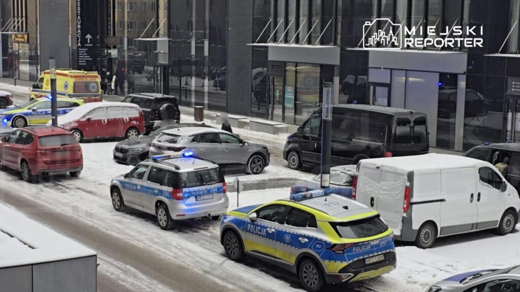 Na ulicy pokrytej śniegiem, pojazdy policyjne i karetka pogotowia zatrzymały się obok zaparkowanych samochodów.