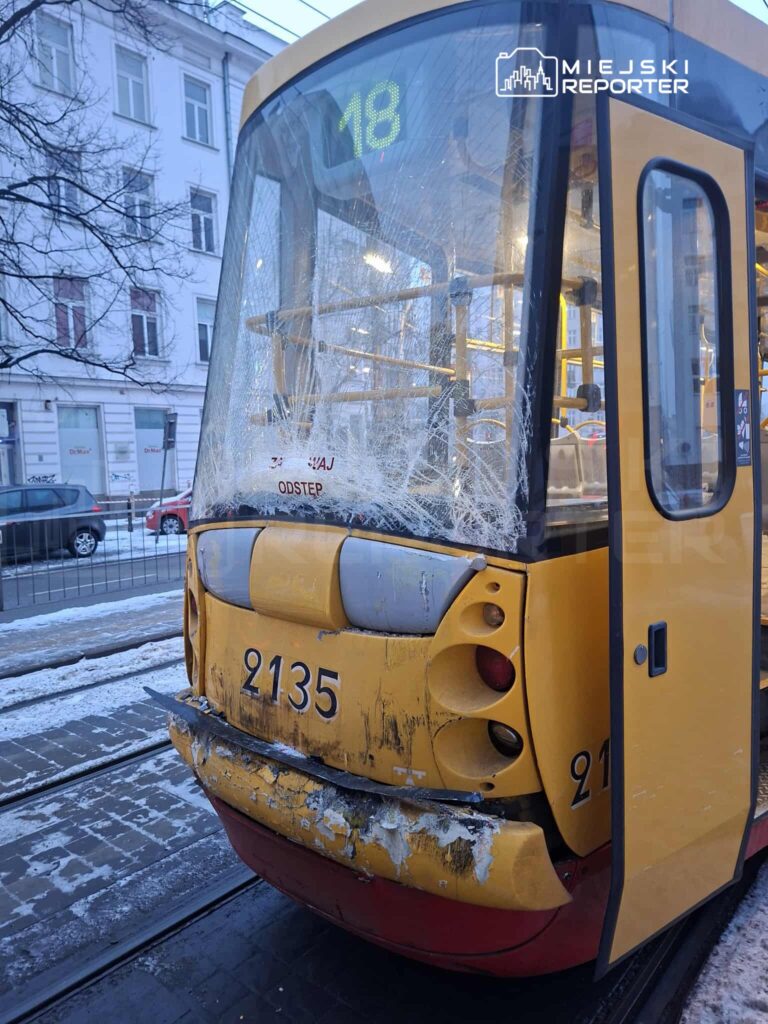 Zniszczony tramwaj z numerem 2135, z pękniętą szybą i uszkodzeniami na tylnej części, stoi na przystanku w zimowej scenerii.