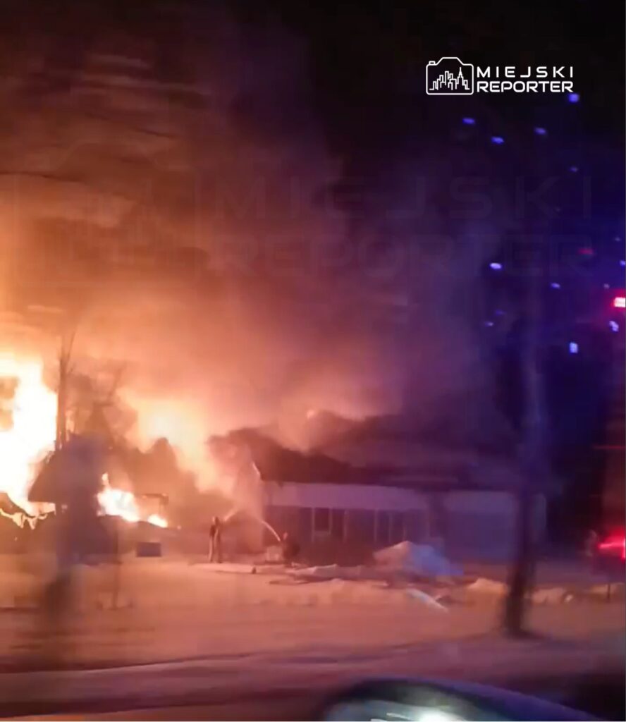 Pożar budynku mieszkalnego, w którym strażacy gaszą ogień, w tle widoczne płomienie i dym.