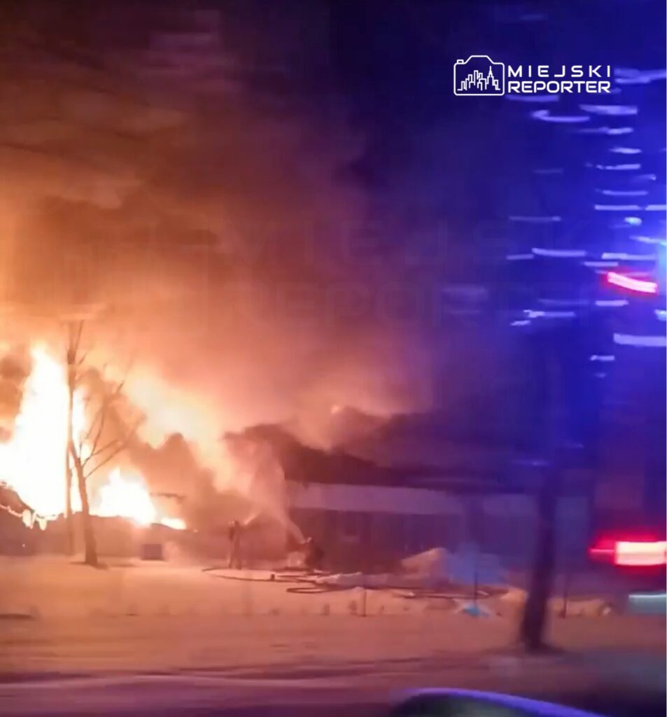 Ogień trawi budynek, a strażacy walczą z płomieniami w otoczeniu zaśnieżonego terenu nocą.