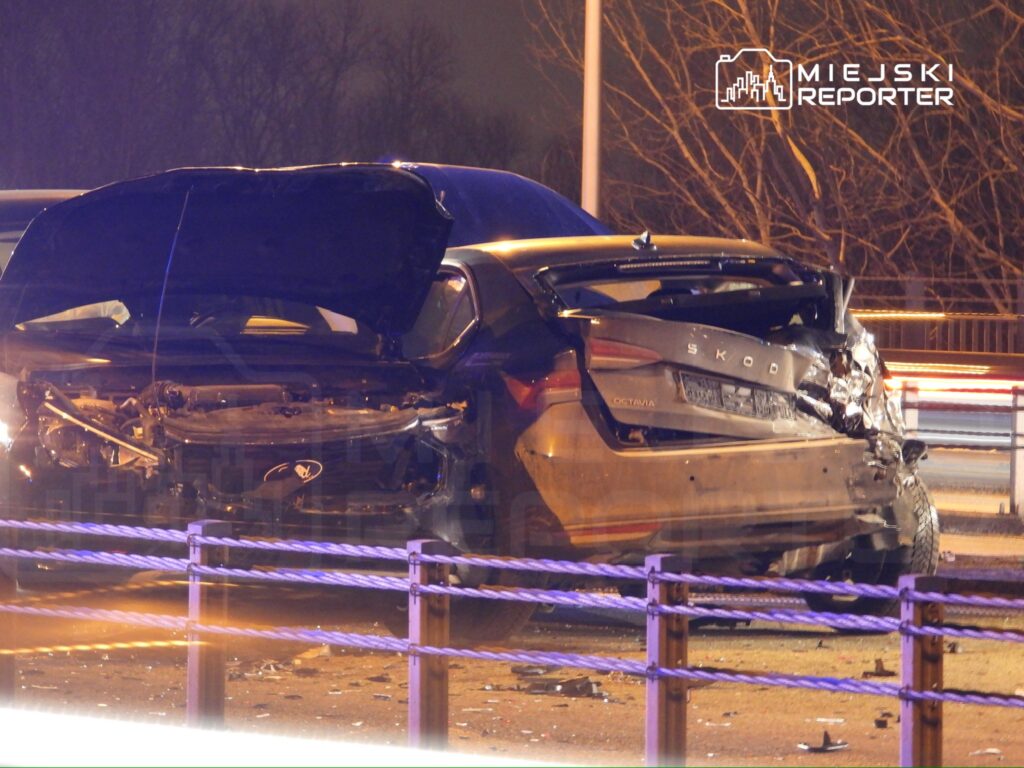 Uszkodzony samochód osobowy marki Skoda leży na poboczu drogi, z widocznymi uszkodzeniami przodu i tyłu.