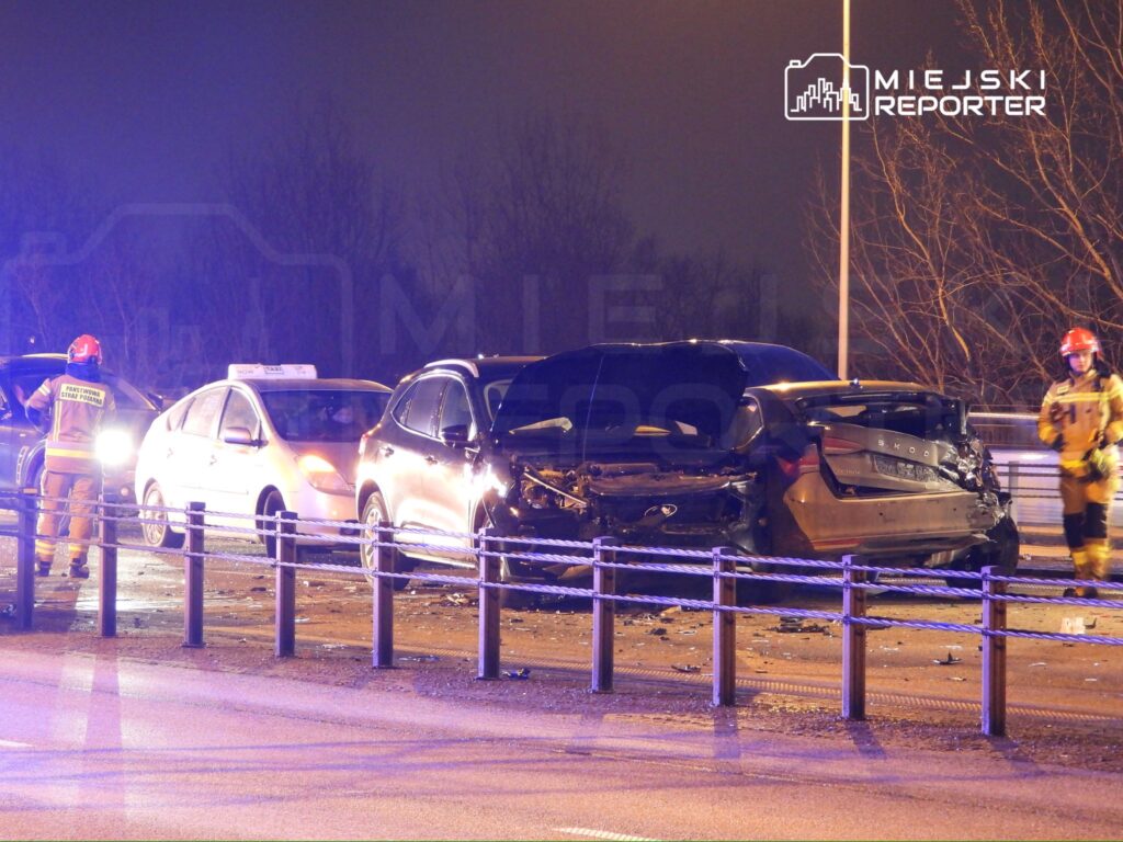 Kierowca w mundurze strażaka bada uszkodzone samochody po wypadku na ruchliwej drodze w nocy.