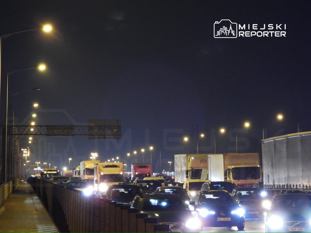 Ruch samochodowy na oświetlonej autostradzie w nocy, z dużą ilością ciężarówek i osobowych pojazdów.