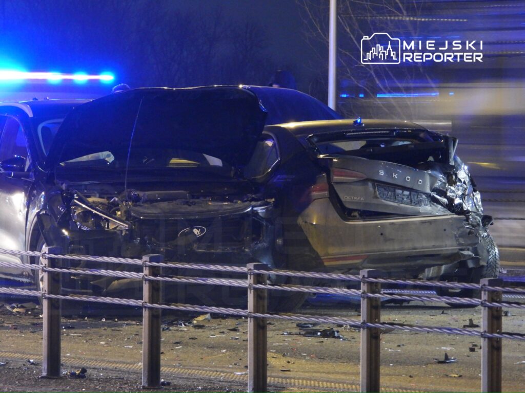 Uszkodzony samochód osobowy marki Skoda Octavia stoi na drodze, w tle policyjne światła.