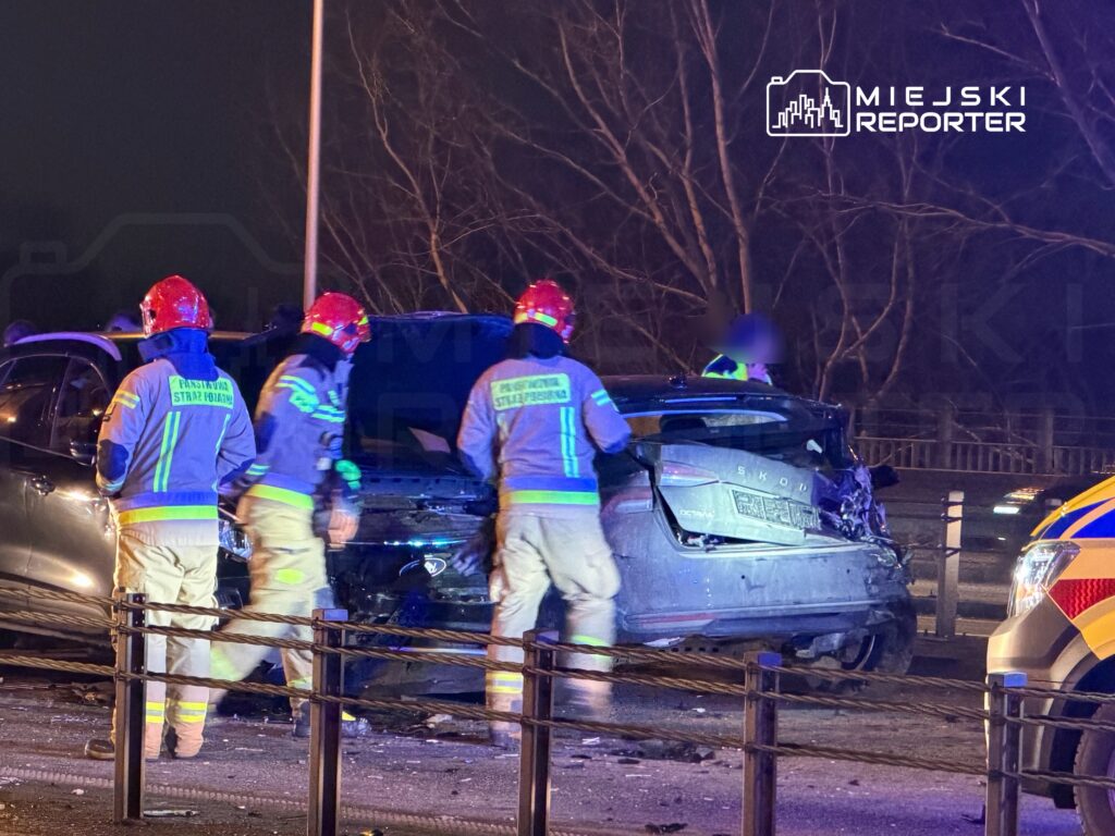 Ratownicy w uniformach i hełmach pracują przy zderzonych samochodach na drodze w nocy.