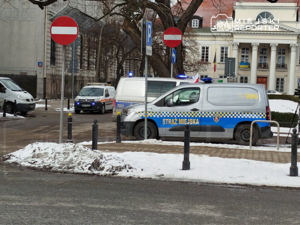 Funkcjonariusze Straży Miejskiej w oznakowanym samochodzie interwencyjnym stoją na ośnieżonej ulicy.