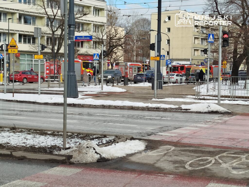 Czerwone samochody strażackie zaparkowane przy ulicy, obok chodnika pokrytego śniegiem, w miejskim otoczeniu.