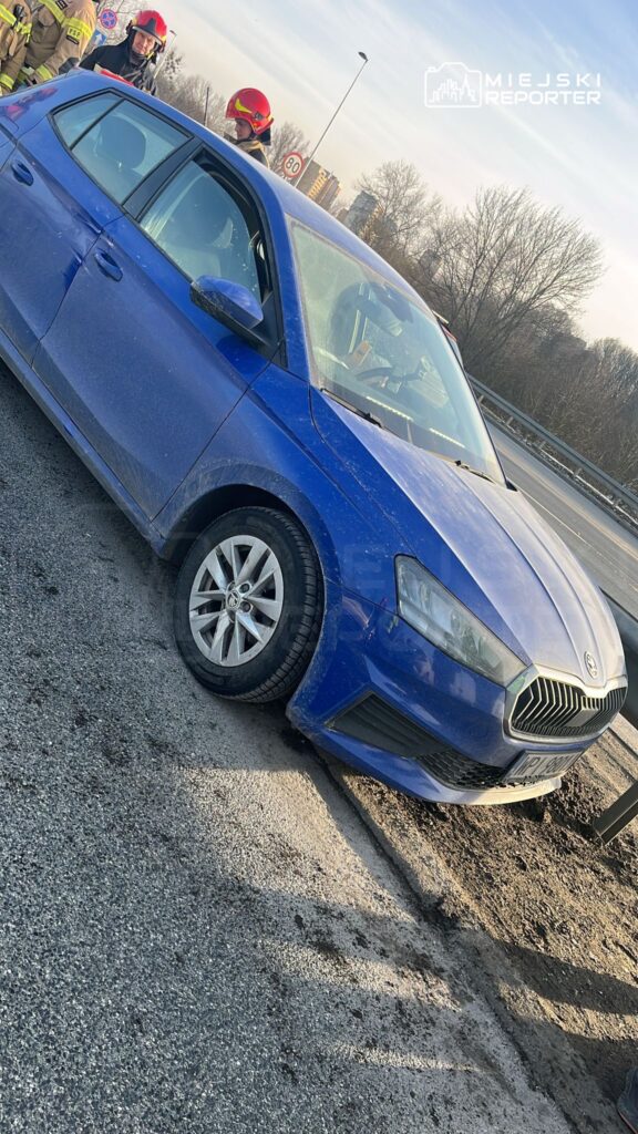 Niebieski samochód osobowy stoi na poboczu drogi, obok grupy ratowników w hełmach.